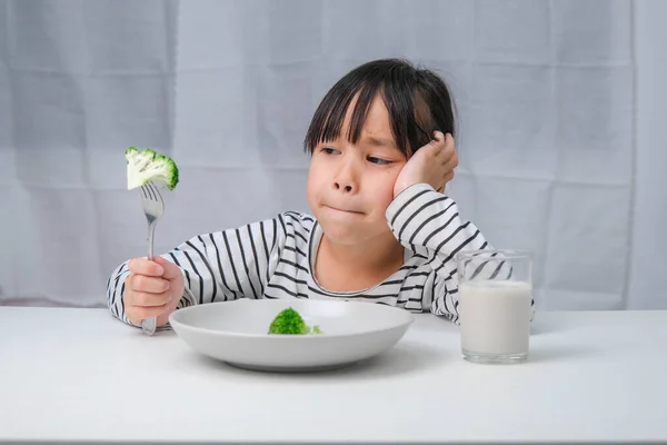 Children don\'t like to eat vegetables. Cute Asian girl refusing to eat healthy vegetables. Nutrition and healthy eating habits for children.
