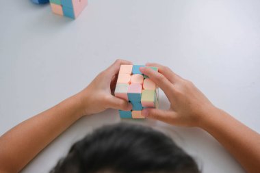 Asyalı küçük şirin kız Rubik küpünü elinde tutuyor ve onunla oynuyor. Rubik Küpü çocuklar için zekayı artıran bir oyundur. Çocuklar için eğitici oyuncaklar