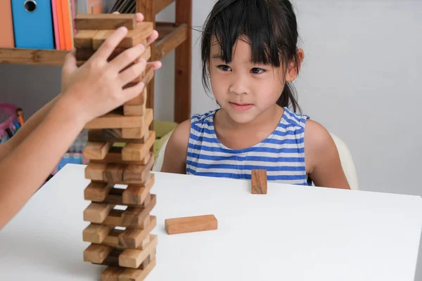 Cute Asian siblings having fun playing Jenga together. Two children playing Jenga board game on table in room at home. Wooden puzzles are games that increase intelligence for children. Educational toys for children.