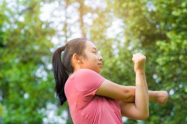 Spor giyimli genç Asyalı kadın, sağlıklı bir yaşam tarzı için parkta egzersiz yapmadan önce esniyor. Genç, sağlıklı bir kadın dışarıda ısınıyor. Sağlıklı yaşam tarzı kavramı.