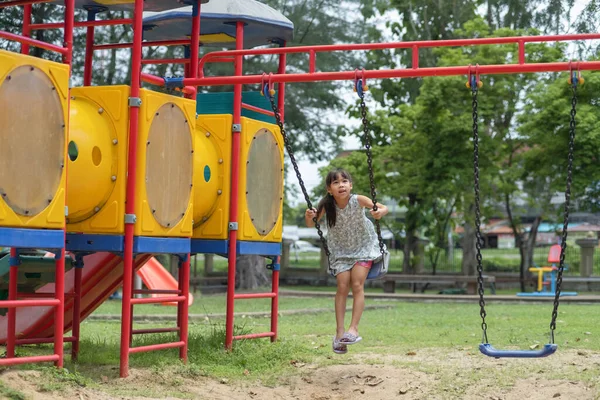 Stock image Happy girl having fun on the swing. Little Asian girl playing at outdoor playground in the park on summer vacation. Healthy activity.