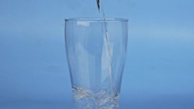 Mavi arka planda izole edilmiş temiz suyu şişeden cama dökerek, cama odaklanarak. İçme suyu kavramı.