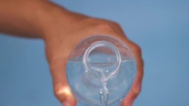 Mavi arka planda el ele tutuşan su şişesi ve dökülen su. Plastik bir şişeden su dökülüyor. Yakın çekim.