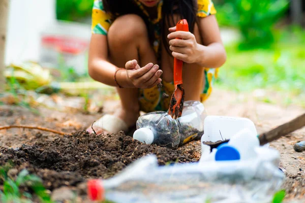 Little girl planting plants in pots from recycled water bottles in the backyard. Recycle water bottle pot, gardening activities for children. Recycling of plastic waste
