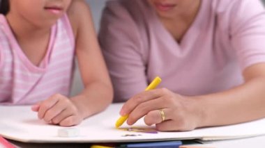 Anne ve kızı pastel boyalarla birlikte çiziyorlar. Yetişkin bir kadın, kızın evde ders çalışmasına ya da resim yapmasına yardımcı olur. Mutlu aile.