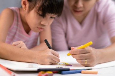 Anne ve kızı pastel boyalarla birlikte çiziyorlar. Yetişkin bir kadın, kızın evde ders çalışmasına ya da resim yapmasına yardımcı olur. Mutlu aile.