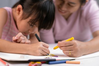 Anne ve kızı pastel boyalarla birlikte çiziyorlar. Yetişkin bir kadın, kızın evde ders çalışmasına ya da resim yapmasına yardımcı olur. Mutlu aile.
