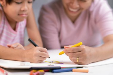 Anne ve kızı pastel boyalarla birlikte çiziyorlar. Yetişkin bir kadın, kızın evde ders çalışmasına ya da resim yapmasına yardımcı olur. Mutlu aile.
