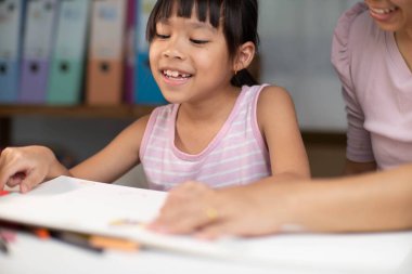 Anne ve kızı pastel boyalarla birlikte çiziyorlar. Yetişkin bir kadın, kızın evde ders çalışmasına ya da resim yapmasına yardımcı olur. Mutlu aile.