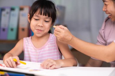 Anne ve kızı pastel boyalarla birlikte çiziyorlar. Yetişkin bir kadın, kızın evde ders çalışmasına ya da resim yapmasına yardımcı olur. Mutlu aile.