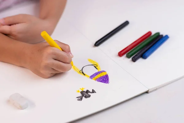 Girl drawing with crayons on a white sheet of paper. Crayons and kids drawing on white background. Close-up of a child\'s hand holding a crayon and drawing, kids Coloring.