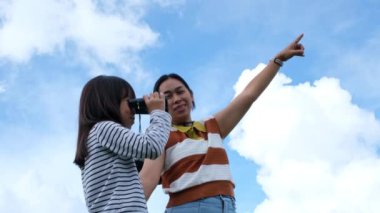 Anne, tatlı küçük kıza güneşli bir günde dağda dürbün kullanmayı öğretiyor. Aktif genç kız gezide dürbün kullanır ve mutlu bir şekilde gülümser..