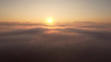 İHA kamerası, güneş doğarken bulutların üzerinde yoğun sis bulutu üzerinde uçuyor. Güneş ufukta yükselene kadar sonsuz bulut denizinin üzerinde yükseliyor..