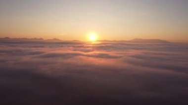 İHA kamerası, güneş doğarken bulutların üzerinde yoğun sis bulutu üzerinde uçuyor. Güneş ufukta yükselene kadar sonsuz bulut denizinin üzerinde yükseliyor..