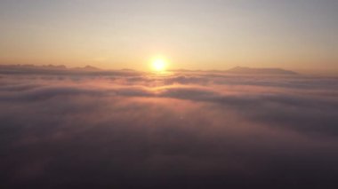 İHA kamerası, güneş doğarken bulutların üzerinde yoğun sis bulutu üzerinde uçuyor. Güneş ufukta yükselene kadar sonsuz bulut denizinin üzerinde yükseliyor..