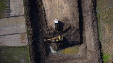 Kurak mevsimde tarım için kullanılmak üzere bir su birikintisi inşa etmek için bir çöp kamyonuna toprak kazmak. Bir kepçenin havadan görünümü işe yarıyor.