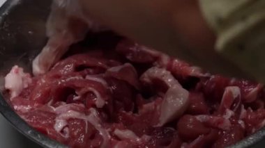 Genç kız, annesinin sukiyaki için kullanılan bir kasede çiğ domuz eti pişirmesine yardım ediyor..