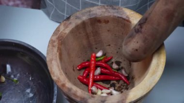 Young woman pounds chili and garlic in a mortar to prepare for cooking.