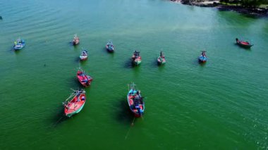 Tayland 'ın güneyindeki küçük bir balıkçı limanına demirlenmiş geleneksel renkli Tayland ahşap balıkçı teknelerinin insansız hava aracı görüntüsü. Denizde bir sürü uzun kuyruklu tekne var.