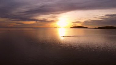 Tayland 'ın tropikal denizinde sabah güneşinin doğuşuna karşı seyreden uzun kuyruklu bir teknenin havadan görünüşü..