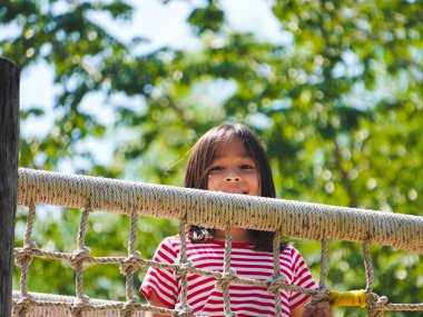 Çocuklar parktaki ahşap oyun parkında oynuyorlar. Mutlu kız yaz boyunca oyun bahçesinde ip ağ köprüsünde oynuyor..