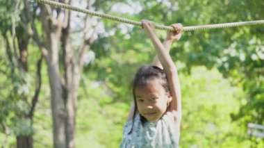 Şirin kız kardeşler açık hava parkında iplerden sallanırken eğleniyorlar. Yaz tatili boyunca oyun bahçesinde oynayan çocuklar.