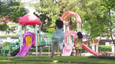 Şirin kızlar açık hava parkında renkli bir kaydırağın üzerinde eğleniyorlar. Yaz tatili boyunca oyun bahçesinde oynayan çocuklar.