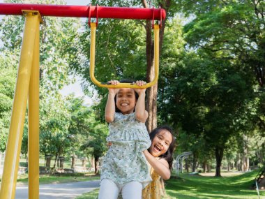 Şirin kız kardeşler parktaki maymun parmaklıklarında takılırken eğleniyorlar. Yaz tatili boyunca oyun bahçesinde oynayan çocuklar.
