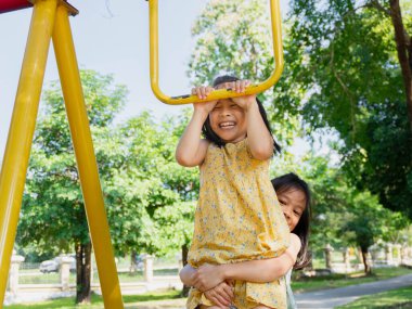 Şirin kız kardeşler parktaki maymun parmaklıklarında takılırken eğleniyorlar. Yaz tatili boyunca oyun bahçesinde oynayan çocuklar.