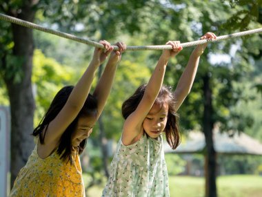 Şirin kız kardeşler açık hava parkında iplerden sallanırken eğleniyorlar. Yaz tatili boyunca oyun bahçesinde oynayan çocuklar.