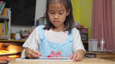 Masada dijital tablet ekranına dokunan sevimli Asyalı kız stilus kalem, tasarım fikri ve evdeki çevrimiçi öğrenme uygulamasını boyama kullanıyor..