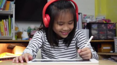 Kulaklık takan sevimli Asyalı kız masadaki dijital tablet ekranlara dokunuyor, stilus kalem, tasarım fikri kullanıyor, evdeki çevrimiçi öğrenme uygulamasını boyuyor..