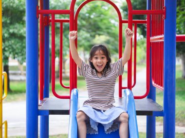 Yaz tatili boyunca parkta oynayan tatlı bir kız. Mutlu kız açık hava parkında renkli bir kaydırağın üzerinde eğleniyor..