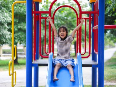 Yaz tatili boyunca parkta oynayan tatlı bir kız. Mutlu kız açık hava parkında renkli bir kaydırağın üzerinde eğleniyor..