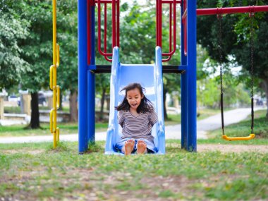 Yaz tatili boyunca parkta oynayan tatlı bir kız. Mutlu kız açık hava parkında renkli bir kaydırağın üzerinde eğleniyor..