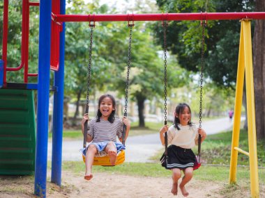 Şirin kız kardeşler parkta salıncakta sallanırken eğleniyorlar. Yaz tatili boyunca oyun bahçesinde oynayan çocuklar.