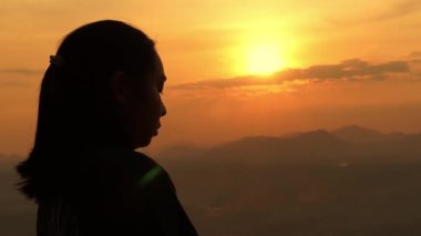Hristiyan bir kadının gün batımında haç tutarak dua edişinin silüeti. Düşünceli bir kadın ellerini kavuşturup dua ediyor. Tanrı 'ya inanç kavramı