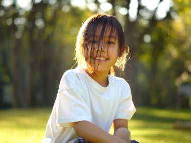 Doğada mutlu küçük bir kız ve ağaçların tadını çıkarıyor. Parkta güzel, sıcak bir gün batımı var..