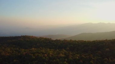 Kış dağlarında güzel bir günbatımı. Batan güneş, akşamları tropikal ağaçlarla kaplı sakin bir dağ manzarasında parlıyor..