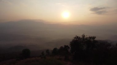 Kış dağlarında güzel bir günbatımı. Batan güneş, akşamları tropikal ağaçlarla kaplı sakin bir dağ manzarasında parlıyor..