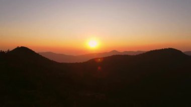 Kış dağlarında güzel bir günbatımı. Batan güneş, akşamları tropikal ağaçlarla kaplı sakin bir dağ manzarasında parlıyor..