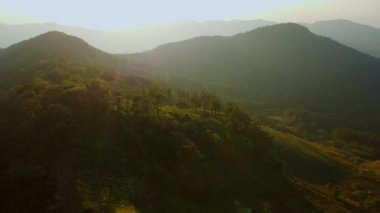 Kış dağlarında güzel bir günbatımı. Batan güneş, akşamları tropikal ağaçlarla kaplı sakin bir dağ manzarasında parlıyor..