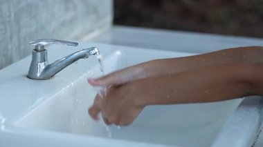 Çocuk ellerini yıkıyor. Umumi bir muslukta temizlenen ellerin yakın çekimi.