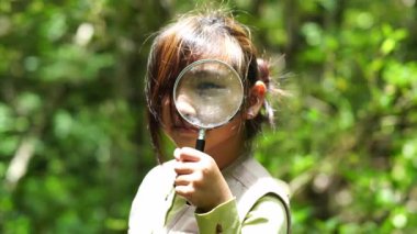 Küçük mutlu bir kız ormanda keşif yapıyor ve elinde büyüteçle böcek arıyor. Macera turizmi ve öğrenme konsepti.