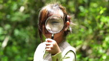 Küçük mutlu bir kız ormanda keşif yapıyor ve elinde büyüteçle böcek arıyor. Macera turizmi ve öğrenme konsepti.