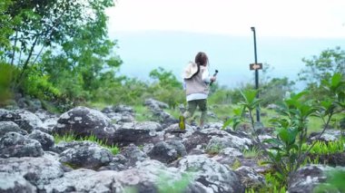 Küçük mutlu bir turist, ulusal bir parkta dağ manzarası arasında video kaydetmek için bir video kamera kullanıyor..