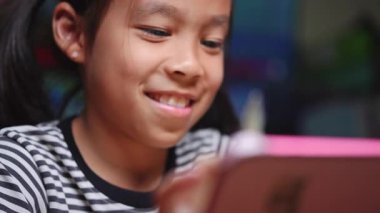 Elektronik tablet ve stil kalem kullanan sevimli Asyalı kız çizimi. Dijital tablet kullanan Asyalı ilkokul öğrencisi evde oturma odasında oturuyor..