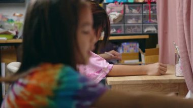 İki ilkokul kızı evdeki masalarında ders çalışıyor. İki tatlı kız öğrenci özenle ödevlerini yapıyor..