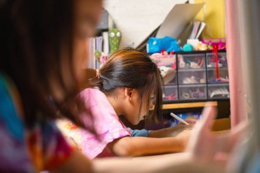 İki ilkokul kızı evdeki masalarında ders çalışıyor. İki tatlı kız öğrenci özenle ödevlerini yapıyor..