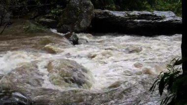 Yağmur mevsiminde yemyeşil bir ormanda çağlayan güçlü bir şelale. Nehir akıntısı güçlüdür ve şiddetli yağıştan sonra su çamurlu hale gelir. Bu da doğanın ham enerjisini gösterir.